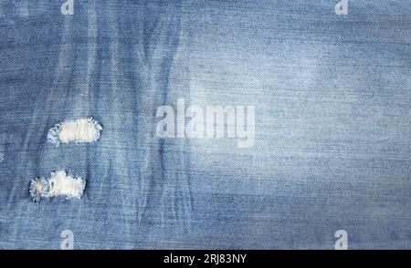 Ripped jeans material of indigo color. Horizontal or vertical background with denim texture of blue color with torn holes Stock Photo