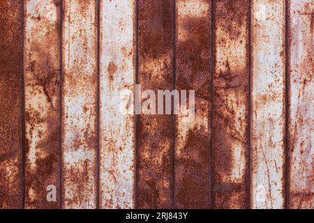 flat texture of rusty corrugated flat thin sheet metal surface with vertical structure and leftovers of white paint Stock Photo