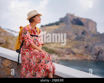 Nice Happy Female Enjoying Greek Islands. Travel to Greece, Mediterranean islands outside tourist season. Having fun at stunning view on sea resort and old town of Lindos on mountain Stock Photo