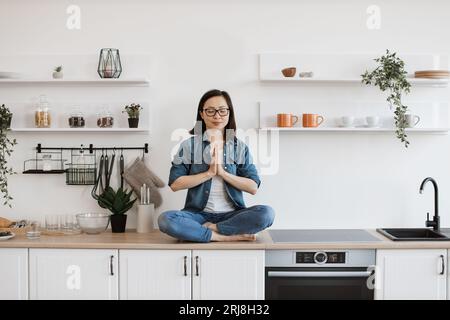 Lady greeting day with namaste in lotus pose on worktop Stock Photo
