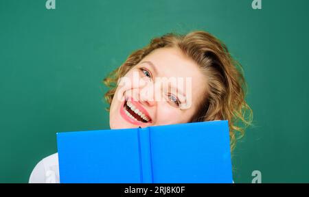 Smiling female teacher with notepad on chalkboard background. School supplies. Back to school. Happy college student girl with open book. Knowledge Stock Photo