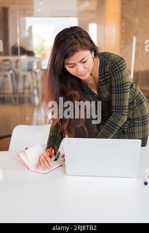 Busy woman taking notes while using laptop Stock Photo