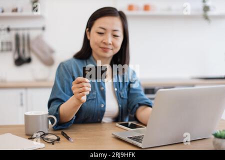 Lady staring at debit card while surfing net on laptop Stock Photo