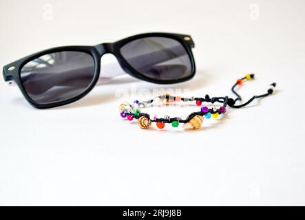 Handmade bracelet made of multi-colored beads and vietnamese seashells of the South China Sea, isolated on white background and blurred sunglasses Stock Photo