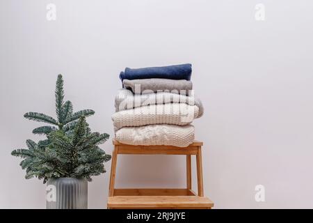 Minimalist winter season composition with knitted sweaters on the wooden stool and fir branches. Stock Photo