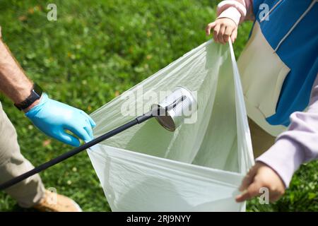 Closeup of father and son putting can in trash bag while eco volunteering outdoors, copy space Stock Photo