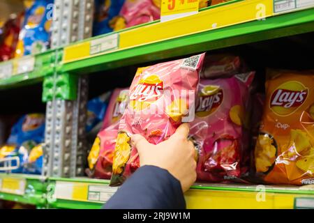 Lays potato chips packaging on store shelf. Man's male hand takes package of chips Lay’s. FMCG brands. Astana, Kazakhstan - 10.24.2022. Stock Photo