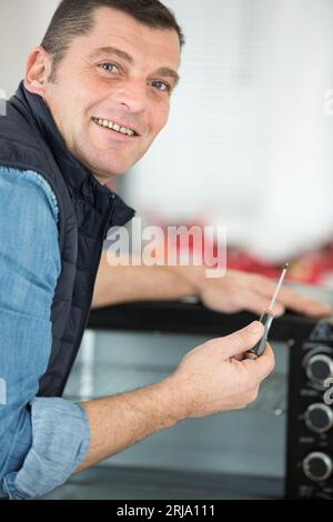 man with screwdriver repairing worktop oven Stock Photo