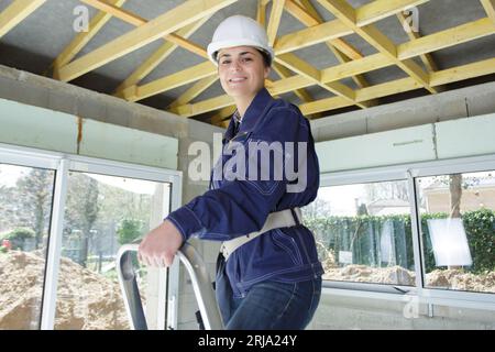 young woman builder stands on a stepladder Stock Photo