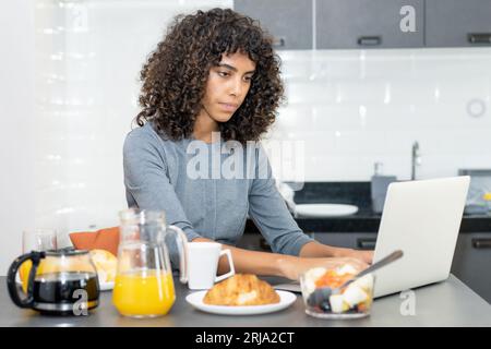 Young latin american woman working at computer in the morning at breakfast Stock Photo