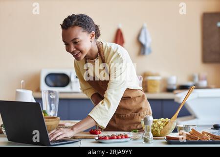 Portrait of smiling black young woman watching cooking video online in kitchen, copy space Stock Photo