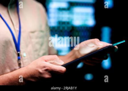 Precise mechanic doing routine system scan, typing data on tablet of needed repairs in blade servers housing advanced data storage equipment supporting complex computational operations, close up Stock Photo