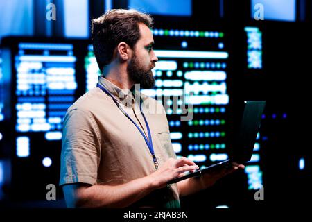 Proficient technician using laptop to check server hub devices. High tech rigs in data storage and cloud computing business service providing processing for several workloads Stock Photo