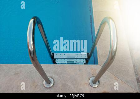 Beautiful pool with a Metal Handrails Descent and blue water at sunset. Swimming and summer rest concept Stock Photo