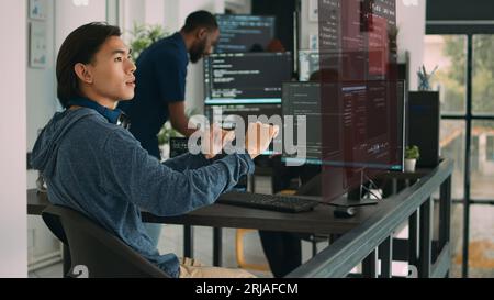 Trained developers helped by AR technology to visualize script in multiethnic office, writing code lines on computer using Java programming languages. Coworkers securing company data Stock Photo