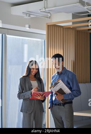 Two diverse coworkers discussing teamwork plan standing in office. Vertical Stock Photo