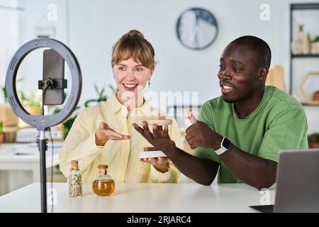 Happy young intercultural couple advertising new self love items they made by themselves at home while guy showing thumb up Stock Photo
