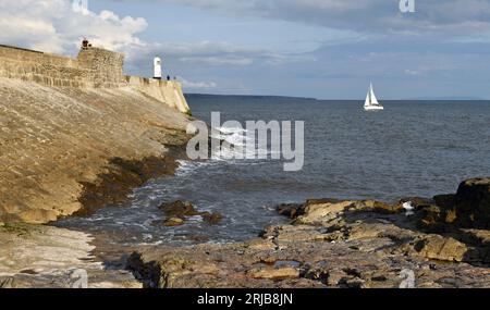 Porthcawl Pier and the famous Lighthouse on a sunny summer evening in July from the beach coast rocks and feauturing a yacht heading into the harbour Stock Photo