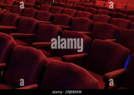 Empty rows of deep red fabric chairs or seats with arm rests in a theater or movie cinema hall. Stock Photo