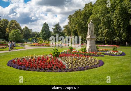 People walk past colourful manicured flower beds and a statue of King Edward VII in Museum Gardens, Beacon Park, Lichfield, Staffordshire, UK. Stock Photo