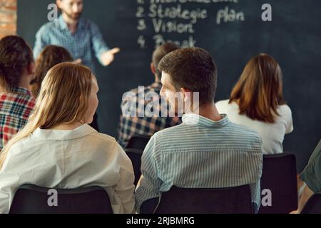 Man coach, speaker giving communicate with audience at business conference. Rear view of business people having workshop. Stock Photo