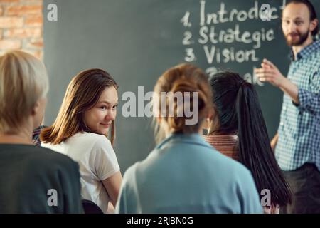 Business and entrepreneurship symposium. Speakers giving talk at business briefing. Rear view of employees communication during meeting Stock Photo