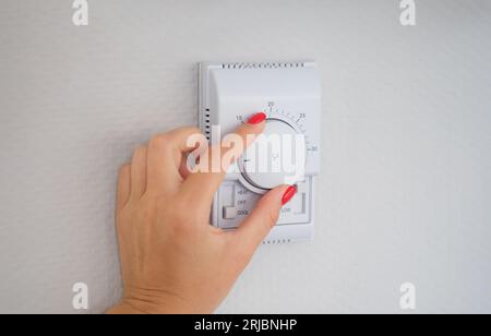 Woman hand adjusts or turns on wall temperature controller controller button Stock Photo