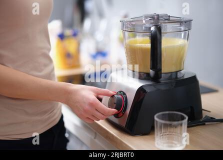 Woman is making smoothie or mixing dough in electric blender Stock Photo