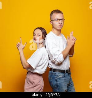 Photo of cheerful people young man and woman in white t-shirt standing back to back against vivid orange studio wall banner background. Stock Photo