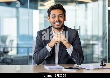 Portrait of young hispanic businessman inside office, boss in business suit smiling and looking at camera, experienced satisfied man at workplace at desk. Stock Photo