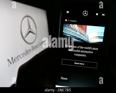 Person holding cellphone with webpage of automotive company Mercedes-Benz Group AG on screen in front of logo. Focus on center of phone display. Stock Photo