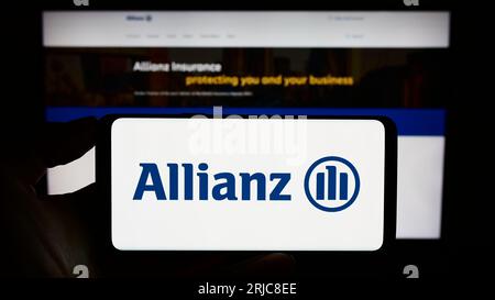 Person holding smartphone with logo of German insurance company Allianz SE on screen in front of website. Focus on phone display. Stock Photo