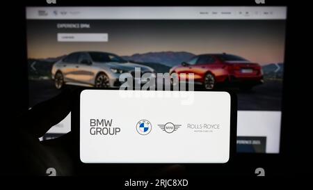 Person holding smartphone with logo of company Bayerische Motoren Werke AG (BMW Group) on screen in front of website. Focus on phone display. Stock Photo