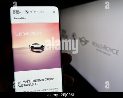 Person holding smartphone with webpage of company Bayerische Motoren Werke AG (BMW Group) on screen with logo. Focus on center of phone display. Stock Photo