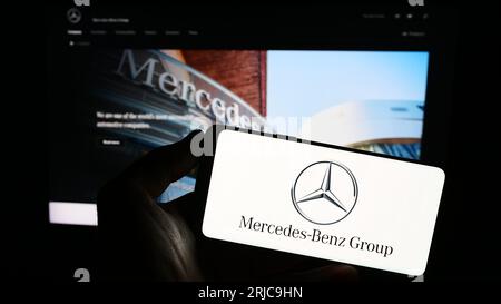 Person holding smartphone with logo of automotive company Mercedes-Benz Group AG on screen in front of website. Focus on phone display. Stock Photo