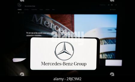 Person holding cellphone with logo of automotive company Mercedes-Benz Group AG on screen in front of business webpage. Focus on phone display. Stock Photo