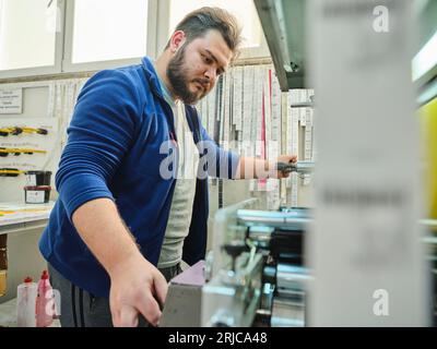 people working in a sticker printing factory. worker uses a stickier printing machine. sticker printer. printing machine working on labels. Stock Photo