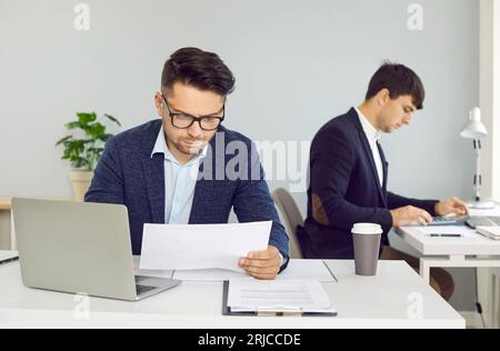 Busy corporate employees sitting at office desks and working with business documents Stock Photo