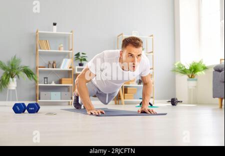 Young attractive man doing push-up exercise lying on yoga mat on the floor at home. Stock Photo