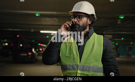 Professional industrial manufacture business industry worker Arabian bearded engineer Indian man in glasses builder in safety uniform hard hat talking Stock Photo