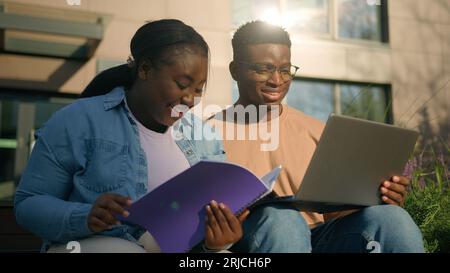 Two friends African American ethnic students woman man girl guy discuss homework university prepare for exams together with computer talking in city Stock Photo