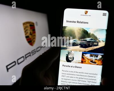 Person holding cellphone with webpage of automotive company Dr. Ing. h.c. F. Porsche AG on screen with logo. Focus on center of phone display. Stock Photo
