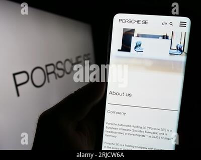 Person holding smartphone with webpage of German company Porsche Automobil Holding SE on screen with logo. Focus on center of phone display. Stock Photo