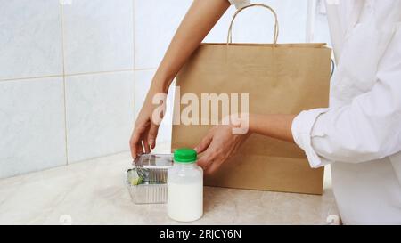 Woman pack ready meal lunch for clients. Delivery of balanced diet food. Chef collect healthy daily menu boxes in plastic takeaway containers. Woman cook on white kitchen. Restaurant business concept Stock Photo