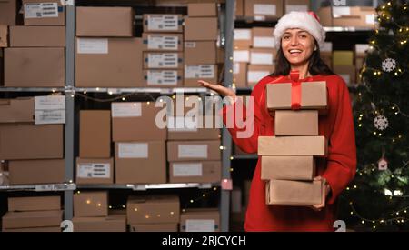 Portrait of female worker wear Santa hat holding boxes inside warehouse Stock Photo