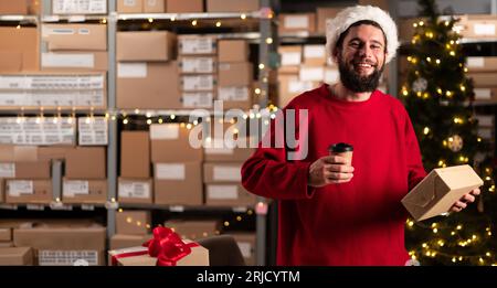 Portrait of male worker holding box inside warehouse drinking takeaway coffee and looking at camera. Stock Photo