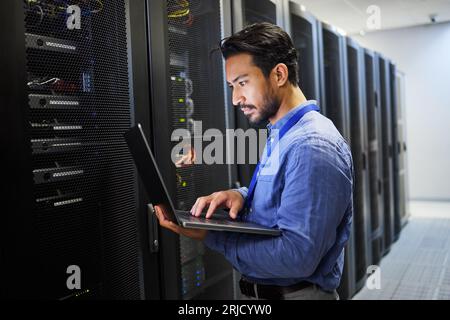 Programming, data center and a man with a laptop for maintenance, cyber security and internet check. Coding, email and an Asian programmer typing on a Stock Photo