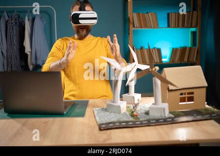 Young man making renewable energy project dummy using laptop and vr goggles at home office Stock Photo
