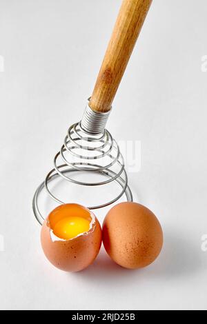 Spiral whisk for beating and two beige chicken eggs on a white background. Cooking an omelette Stock Photo