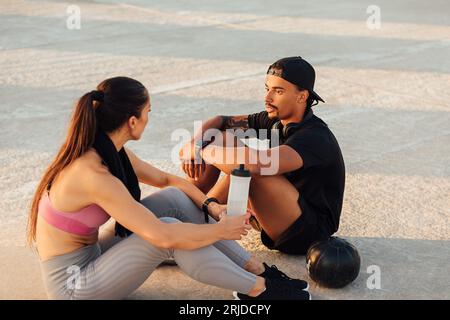 Fitness couple taking a break during workout sitting together on the roof at sunset Stock Photo